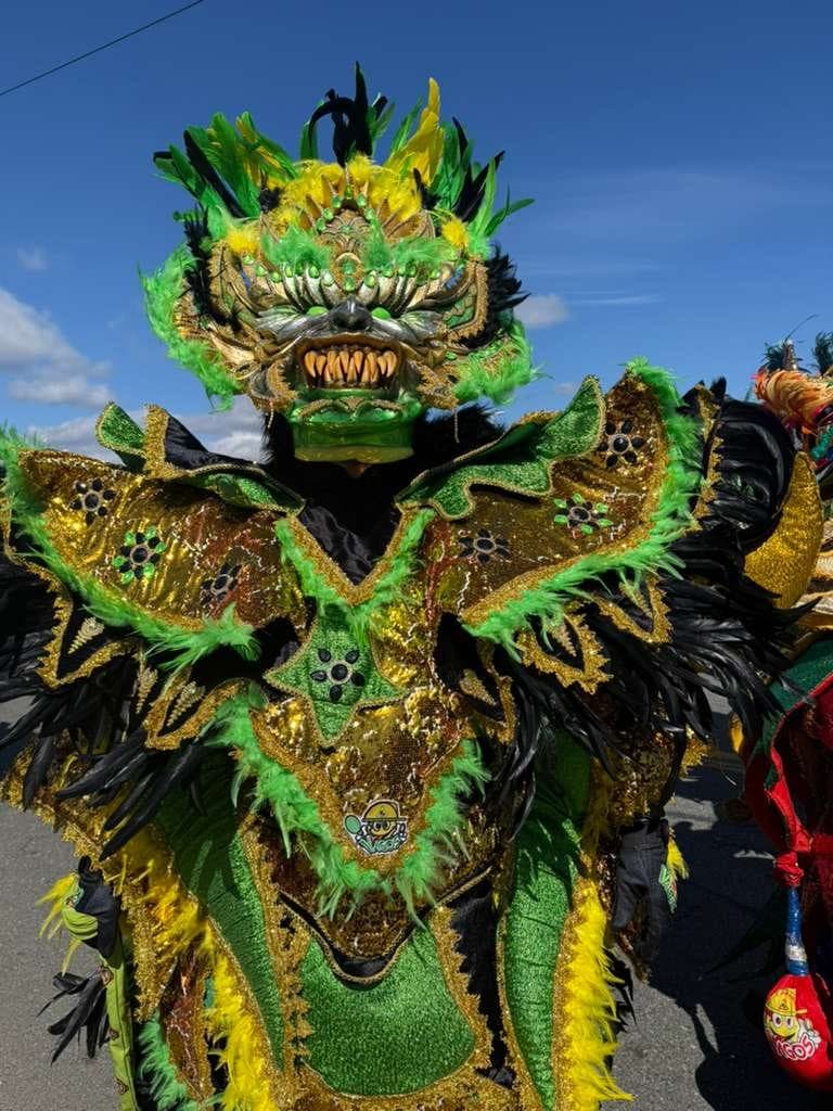 A performer in an elaborate green horned Diablo Cojuelo costume with feathered wings under a clear blue sky