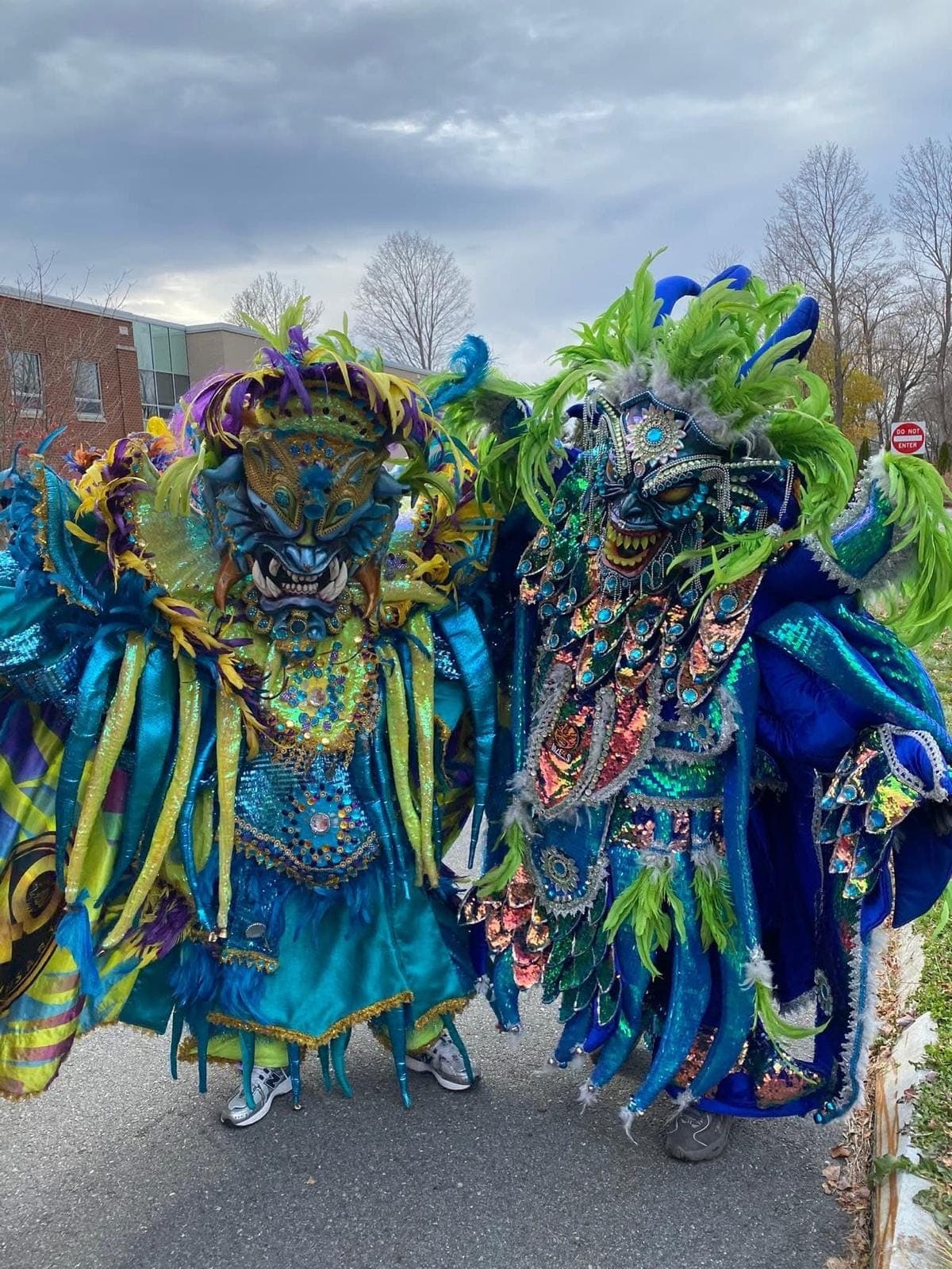 Two performers in blue and green feathered Diablo Cojuelo masks and sequined capes