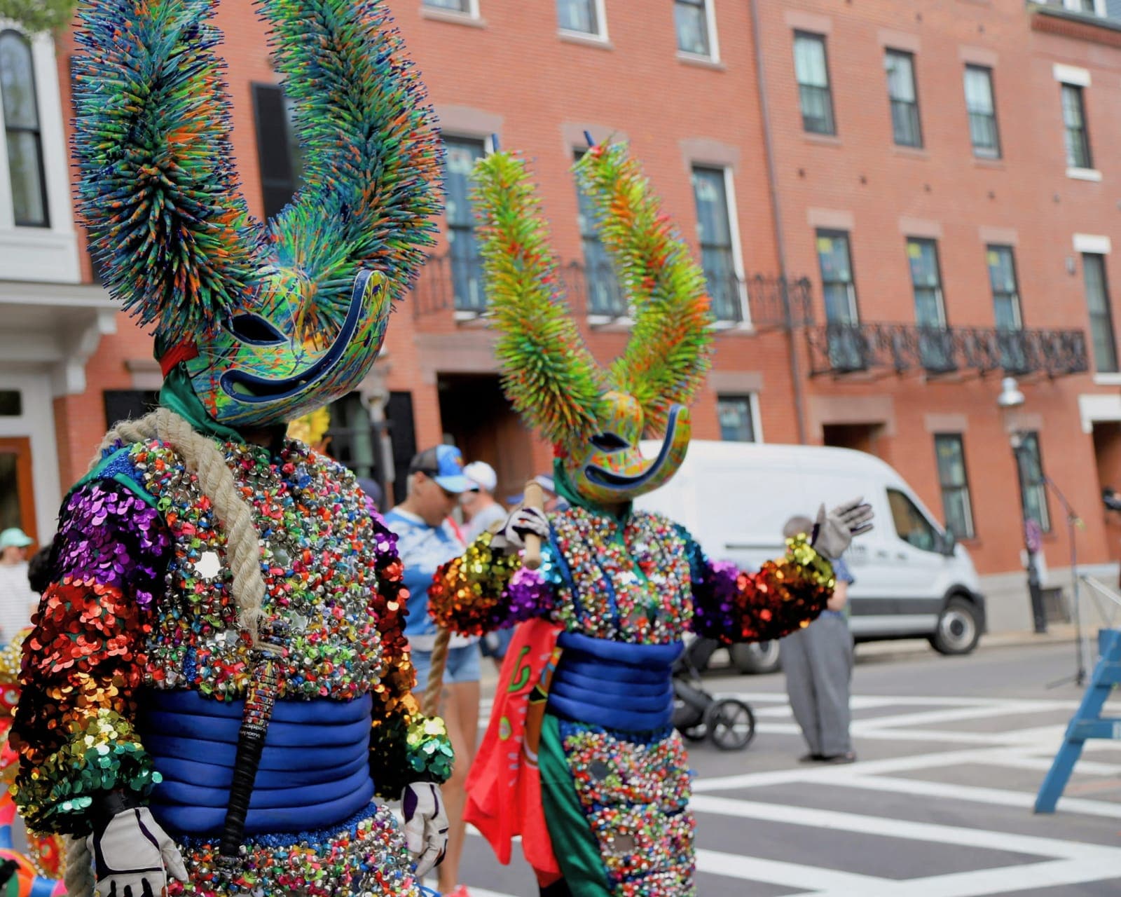 Two performers in rainbow spiky-horned costumes, one waving to the crowd