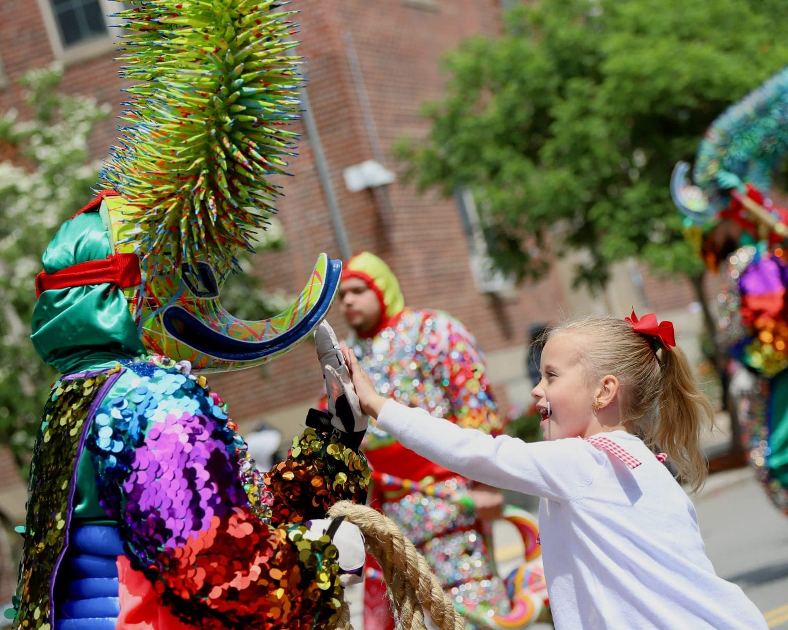 A performer in a green spiky-sequined costume high-fives a young girl during the parade