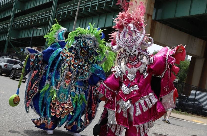 A teal-and-pink feathered carnival devil beside a magenta-plumed performer