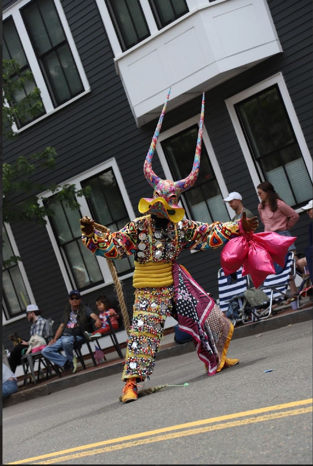 A performer in a purple and gold horned costume dancing in the middle of the parade route