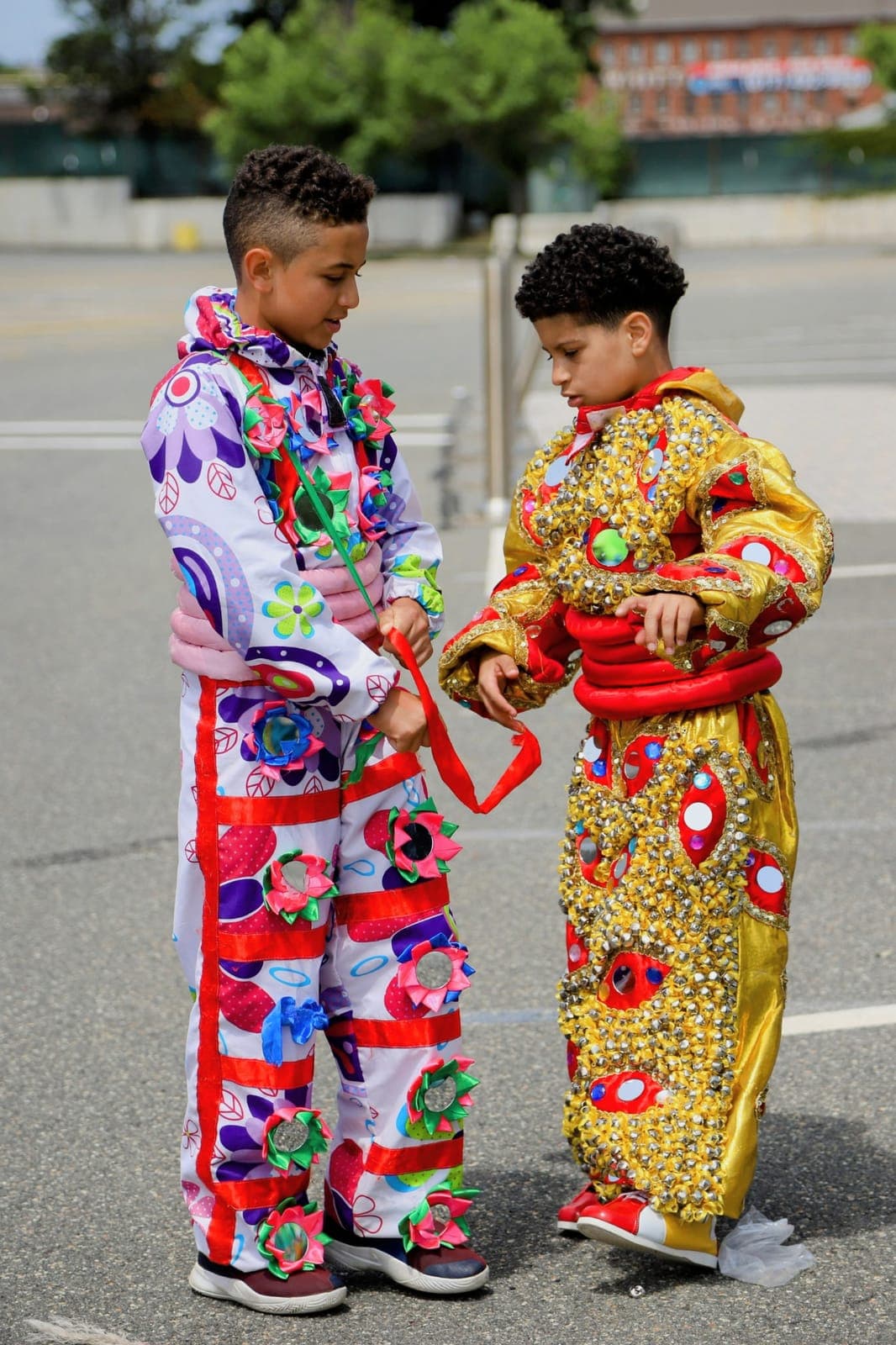Two children in matching floral-beaded carnival suits face each other in the street