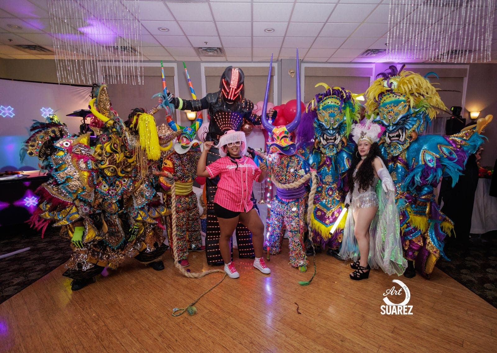 ACM performers and community members gather in colorful Carnaval costumes at an indoor celebration