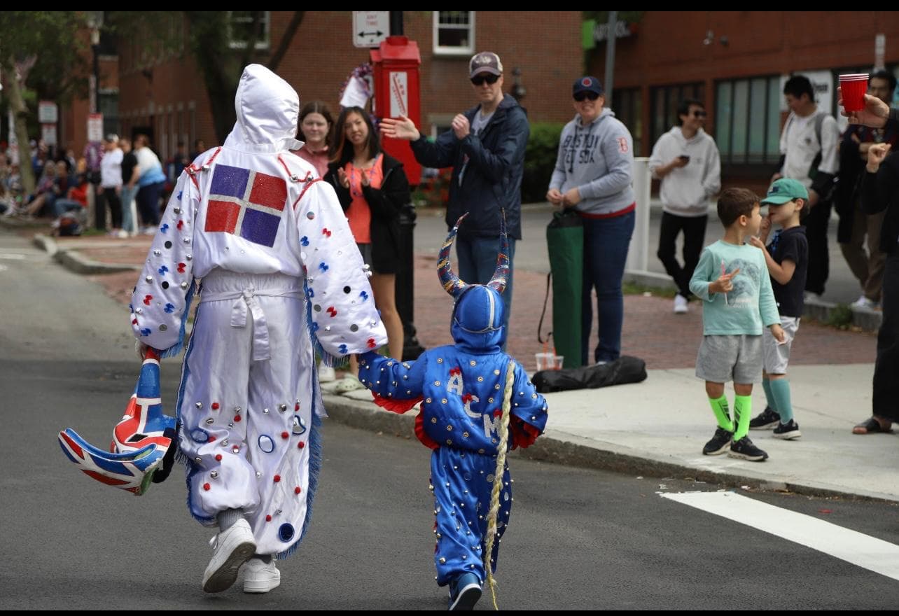 An adult and child ACM performer in coordinated white and blue Carnaval costumes greet families along a parade route